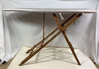 Side view of the vintage wooden ironing table showing the folding X-legged frame and padded top.