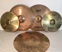 Five cymbals laid out on white drape: two Sabian SBR hats, three Zildjian cymbals.