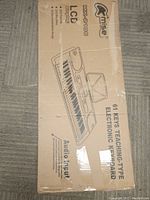 Closed cardboard box showing Mise MK-210661 branding and product specifications including 61 keys, teaching-type keyboard, LCD display, 255 rhythms, and 24 demo songs.