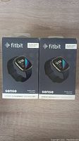 Two sealed Fitbit Sense boxes side by side on wood surface