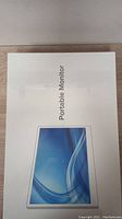 Front of the factory sealed white box showing image of the portable monitor with blue screen on front and text Portable Monitor.