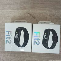 Front view of two boxed Samsung Galaxy Fit2 smartwatches showing product image and 'Fit2' branding.