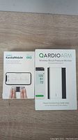 Photo of boxed AliveCor KardiaMobile EKG device and QardioArm Wireless Blood Pressure Monitor, showing front of packaging.