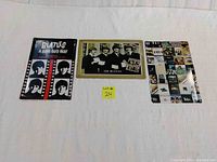 Three tin plaques laid out on a flat surface showing different Beatles-themed images including 'A Hard Day's Night' cover, group photo, and album/magazine collage.