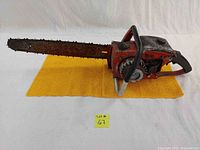 Side view of the full chainsaw on a yellow towel showing condition including rust and chipped paint on the bar, chain, and body.