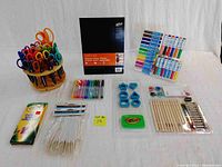 Full view of children's art supplies displayed on white background including scissors, paper, pastels, feathers, cutters, markers, paintbrushes.