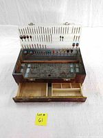 Open wooden case showing assortment of rotary bits and sanding bands organized in a molded plastic insert above a pull-out drawer.