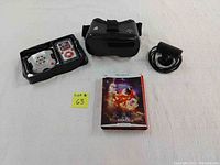 Four electronic gaming items on white background including a virtual reality headset, poker game console with remote, black charger/PlayStation Move camera, and View-Master VR Space Experience pack box.