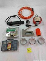Lot displayed on white surface, showing all 10 items clearly including power strip, orange extension cord, stapler, door handles, string, duct tape rolls, and nail organizer.
