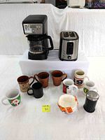 Photo showing Hamilton Beach coffee maker, Hamilton Beach toaster, assorted mugs, coffee filters, and black glass sugar dispenser.