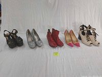 Full view of all five pairs of shoes lined up from left to right: black platform heels, silver sequin heels, red ankle boots, nude and raspberry heels, nude and black booty heels.
