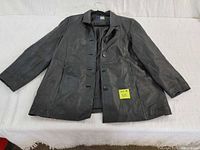 Front view of men's black leather long coat laid flat; buttons visible and coat shows wear.