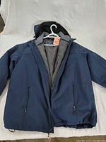 Front view of Izod men's XXL winter jacket, navy blue with hood and zippered pockets, displayed on hanger.