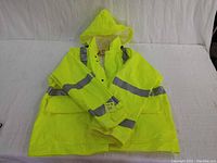 Full view of neon yellow high-visibility rain jacket with reflective grey stripes on arms and across torso, laid flat with hood visible