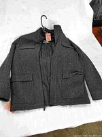 Full view of charcoal grey men's jacket laid flat showing front and pocket details.