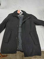 Full view of the dark gray wool zip-up jacket laid flat, showing front, flap pockets, and button closure.