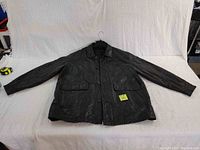 Full view of black leather jacket showing front button closure, two flap pockets, and overall condition.