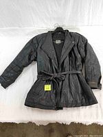 Front view of black leather men's jacket, showing tie waist belt and zipper closure on a white background.