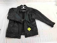 Full view of black leather men's jacket laid flat, showing exterior front including zip closure and snap buttons, on white surface.