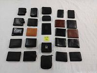 Top view of 25 assorted men's wallets arranged on a surface. Various sizes, mostly black leather with some brown and tan. Visible surface wear and water damage.
