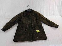 Photo of men's dark army green leather and suede jacket, arms spread horizontally on white backdrop with hanger inside collar.