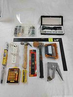 Photo showing the entire lot of 12 tools including stapler, hammer, level, screws, ruler, power bar, screwdriver kit, and others arranged on a white backdrop.