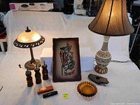Wide shot of all items displayed together on a white cloth including two lamps, two wooden grinders, the abstract painting, the amber ashtray, the swan harmonica, and the stone object.