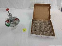 Photo showing the shot dispenser with six colored shot glasses on tray and box containing 32 clear shot glasses.