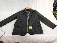 Full view of men's black leather jacket laid flat showing front, collar, sleeves, and pockets on white backdrop.