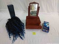 Wooden vanity mirror with drawer in front center, blue and black synthetic curly wig on left, and boxed Oral-B Pro 1000 rechargeable toothbrush on right.