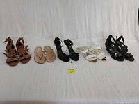 All five pairs of women's shoes displayed together in a row on a white background showing variety including heeled sandals, flip flops in brown, black, white and rose gold colors.