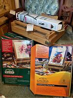 Photo of wooden student field easel partially assembled and two boxed complete easel painting sets in original packaging: Winton by Winsor & Newton and Galeria sets.