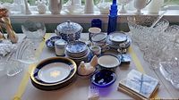 Overview of porcelain and glassware items arranged on table including plates, bowls, mugs, and decorative figurines
