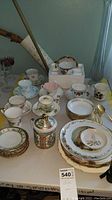 Full display of assorted china items including plates, cups, bowls, and a lidded mug on a table