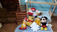 Photo of wooden doll furniture and nine plush toys arranged on cushion and floor. Shows full lot contents including doll bed, chair, and all plush characters.