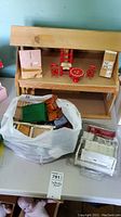 Photo of wooden dollhouse with vintage red painted furniture pieces on middle shelf and additional dollhouse furniture, some in plastic packaging on table below