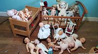 Shelf with multiple vintage dolls, two wooden doll beds, cast iron and wooden doll chairs, and small doll stroller scattered on floor and beds
