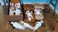Dolls in three wooden cradles including baby dolls and Cabbage Patch dolls, plus small plastic figures on the floor