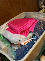 Plastic storage tote filled with various fabric remnants including bright pink and dark blue floral patterned fabrics.