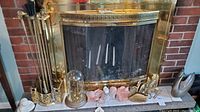 Full view of fireplace with brass fireplace tools, anniversary clock, brass animal figures, terracotta cherubs, and Madonna figurine arranged on hearth.
