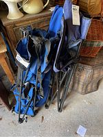 Two blue folding canvas chairs folded and leaning against furniture, showing wear on fabric and metal frames.