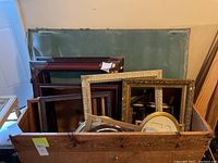 Assorted picture frames stacked in a wooden crate, various sizes, styles, and finishes visible
