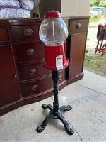 Full view of the replica gumball machine showing glass globe, red metal base, and black metal stand in a garage setting.