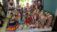 Wide view of over 50 vintage dolls from various cultures displayed on a table by a window.