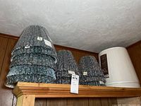 Photo of 11 patterned blue ruffled lampshades and 1 white pleated lampshade on a wooden shelf.