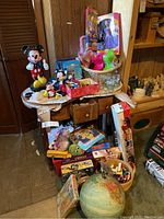 Overview of table and floor showing Mickey Mouse collectibles, Aladdin dolls, Casio keyboard, globe, miscellaneous items