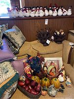 Wide shot of white snowmen figurines, brown basket, orange pumpkins, and various fall harvest decor on couch and shelf
