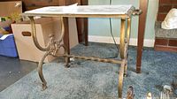 Full view of side table displaying cast iron legs and brass-toned finish with the papered wooden top.