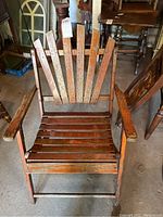 Front view of wooden folding chair with vertical slatted back, horizontal seat slats, and armrests, showing weathered and worn wood finish.