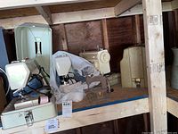 Overview of four vintage portable sewing machines on wood shelf including Singer and Kenmore models, some with carrying cases and cords.
